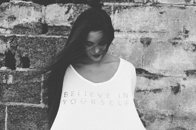 A woman looked down at her shirt and what does it say "believe in yourself"
